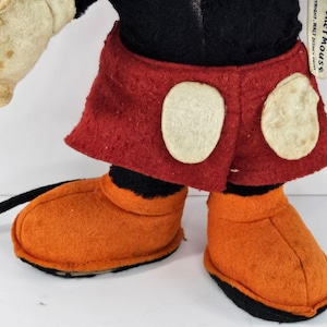 May include: A vintage Mickey Mouse plush toy with black fur, red shorts with white circles, and orange felt shoes. The toy has a tag that reads "Copyright Walt Disney Productions".