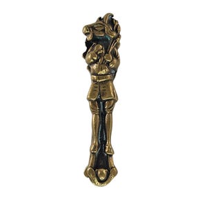May include: A vintage brass nutcracker shaped like a man. The nutcracker depicts a man in period clothing, with a textured finish and a dark patina. The figure's head is at the top, and the handle is at the bottom. The item is made of brass.