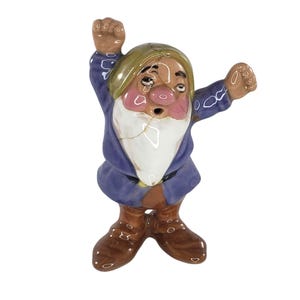 May include: A ceramic figurine of a dwarf with arms raised. The dwarf wears a blue tunic, brown boots, and a green cap. The figurine has a white beard and a surprised expression. The figurine has cracks.