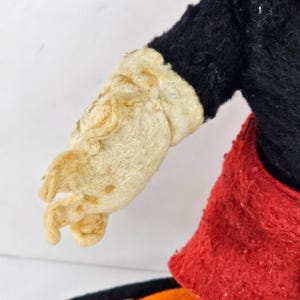 May include: Vintage plush toy with a black and red outfit. The toy has a white felt glove with a worn appearance.