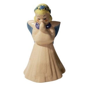 May include: A ceramic figurine of a praying angel with blue wings, a yellow crown of flowers, and a white dress.