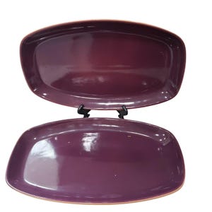 May include: A set of two purple ceramic serving platters with a slightly rounded rectangular shape. The platters are glazed and have a glossy finish.