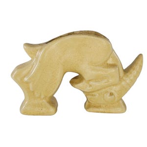 May include: A ceramic rhinoceros sculpture in a pale yellow colour. The rhinoceros is depicted in a crouching position with its head lowered.