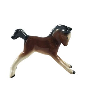 May include: A brown and white ceramic figurine of a horse foal. The foal is standing on its hind legs with its front legs raised. The foal has a black mane and tail.