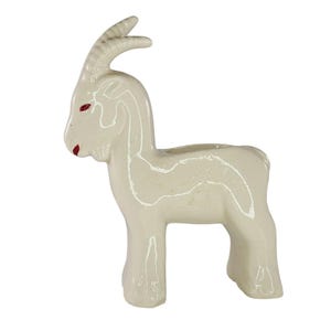Peut inclure: Une figurine de chèvre en céramique blanc cassé brillant avec une ouverture creuse sur le dos. La chèvre présente des cornes incurvées, des yeux peints en rouge et une bouche peinte en rouge. La surface a une finition lisse et réfléchissante.