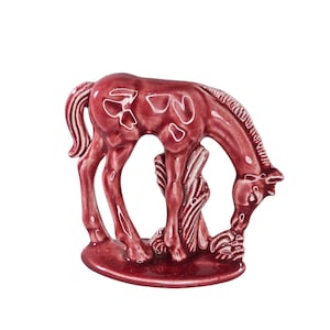 May include: A maroon ceramic horse figurine in a grazing pose. The horse has white accents and is standing on a round base. The figurine is a decorative item.