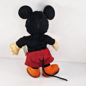 May include: A vintage plush Mickey Mouse toy with black fur, red shorts, and orange shoes. The toy has a tag that reads "Disney Mickey Mouse".