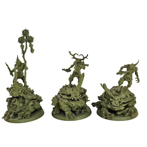 May include: Three green miniature figurines of fantasy creatures. Each figure stands atop a textured base, with one holding a staff and the others in dynamic poses. The figures are detailed with horns and grotesque features.