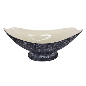 May include: A boat-shaped decorative bowl with a speckled dark blue exterior and a cream-coloured interior. The bowl sits on a rounded pedestal base. The speckled design gives the bowl a unique, textured appearance.