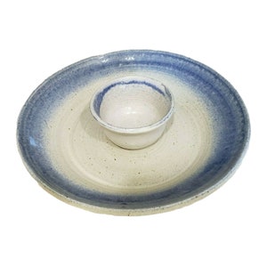 Può includere: Un piatto da portata in ceramica bianca con un bordo blu e una ciotola bianca più piccola al centro. Il piatto è perfetto per servire spuntini o salse.