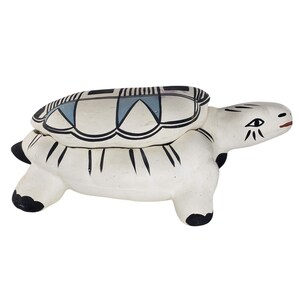 Può includere: Una tartaruga in ceramica bianca con disegni dipinti in nero e blu. La tartaruga è una scatola con cerniere e un coperchio.