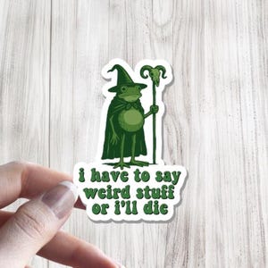 May include: A green sticker featuring a frog dressed as a wizard, holding a staff. The sticker has the text "I have to say weird stuff or I'll die" in green. The sticker is on a white background.