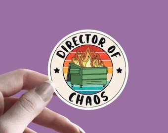 May include: A round sticker with a vintage-style design featuring a dumpster on fire with the text "Director of Chaos" in a circle around it.