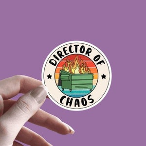 May include: A round sticker with a vintage-style design featuring a dumpster on fire with the text "Director of Chaos" in a circle around it.