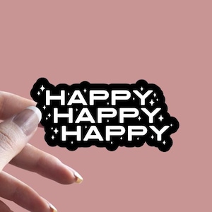 May include: A black sticker with the word "HAPPY" repeated three times in white, outlined in black. The sticker has star-shaped accents and is held against a pink background. The sticker is from Thee Sticker Shop.