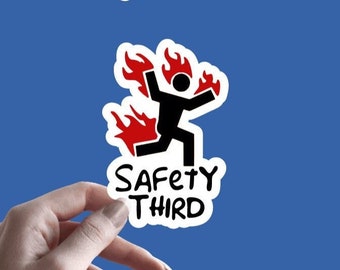 Puede incluir: Una pegatina blanca con una figura de palo negra corriendo con llamas rojas saliendo de su espalda. El texto "SAFETY THIRD" está escrito debajo de la figura.