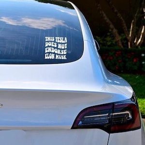 May include: A white Tesla Model 3 with a sticker on the rear window that reads "This Tesla does not endorse Elon Musk."