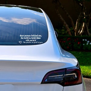 May include: A white car with a rear window sticker that reads "dear person behind me, the world is a better place with you in it. ♡the person in front of you"