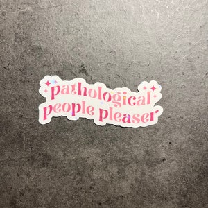 Pode incluir: Adesivo rosa e branco com o texto "pathological people pleaser" com detalhes de glitter.