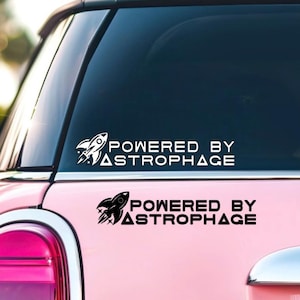 May include: Pink car with two white and black "POWERED BY ASTROPHAGE" rocket ship decals on the rear window and body. The decals feature a rocket ship graphic and text, suitable for space enthusiasts.