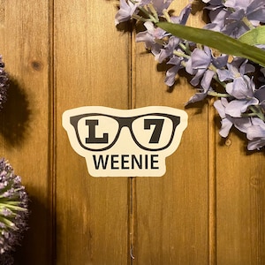 May include: White sticker with a black pair of glasses with the letters "L7" on the lenses and the word "WEENIE" below.