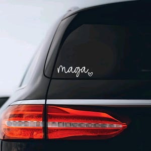 May include: A black car with a white vinyl sticker on the rear window that says "maga" with a small heart next to it.