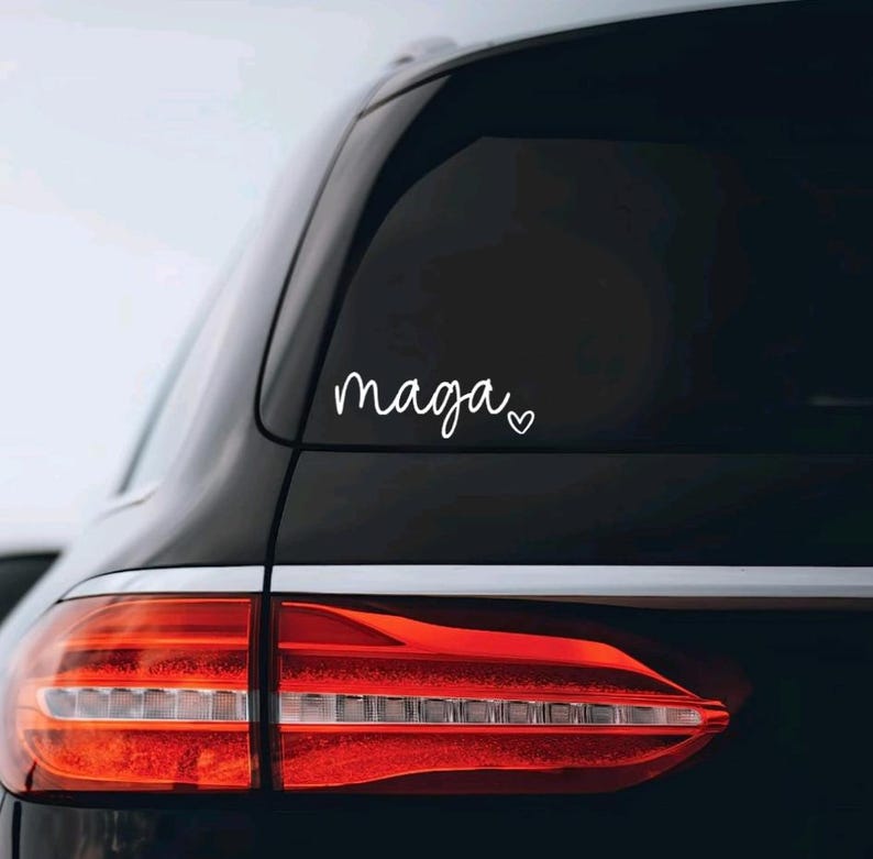 May include: A black car with a white vinyl sticker on the rear window that says "maga" with a small heart next to it.