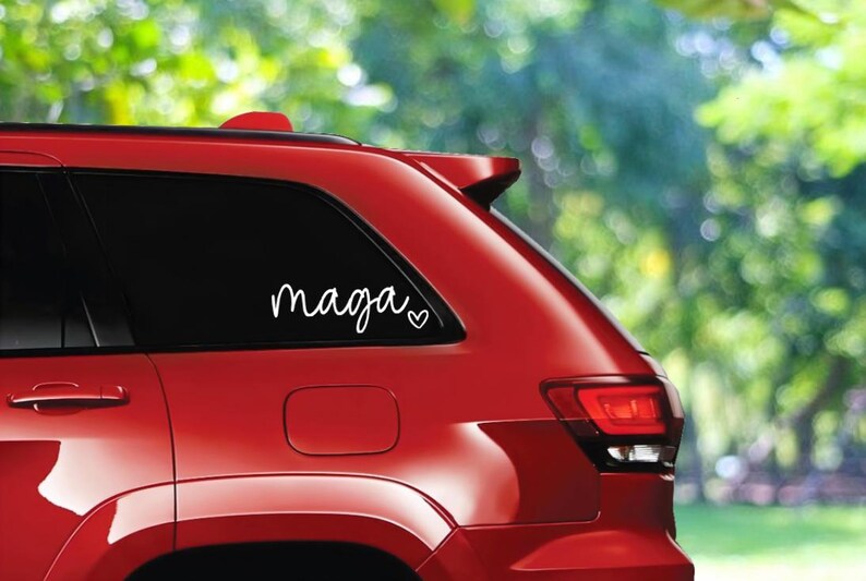 May include: A red car with a white vinyl decal on the rear window that says "maga" with a small heart next to it.
