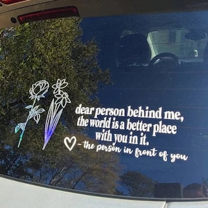 May include: A white vinyl sticker with a floral design and the text "dear person behind me, the world is a better place with you in it. - the person in front of you".