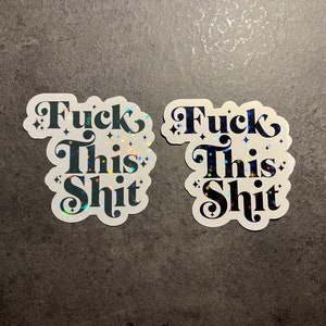 May include: Two stickers with the phrase "Fuck This Shit" in a bold, decorative font. The stickers have a white background with a holographic, glittery effect. The text is dark teal with star accents.