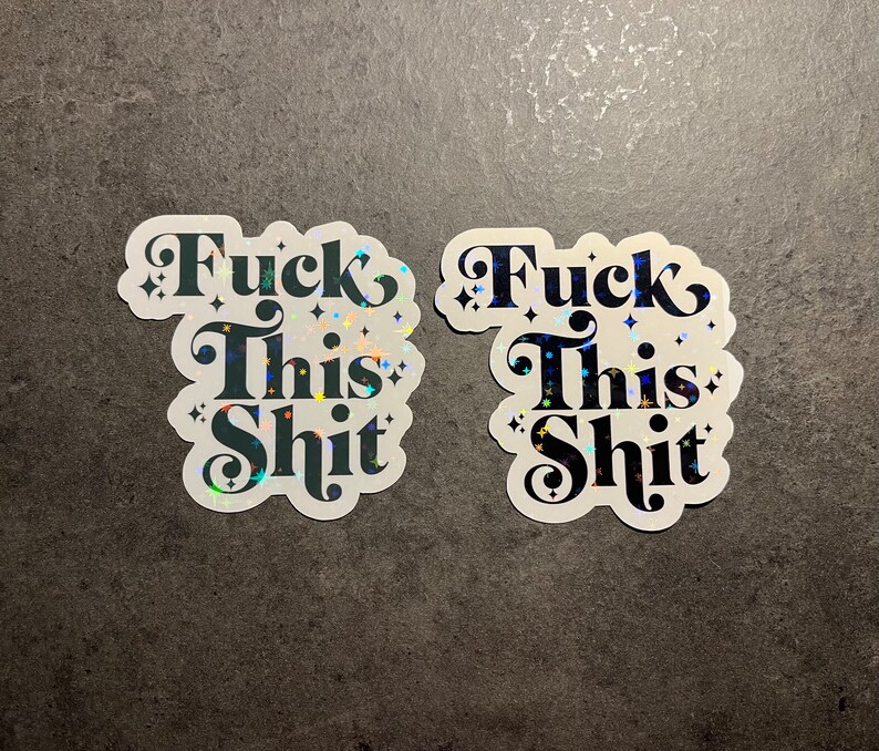 May include: Two stickers with the phrase "Fuck This Shit" in a bold, decorative font. The stickers have a white background with a holographic, glittery effect. The text is dark teal with star accents.
