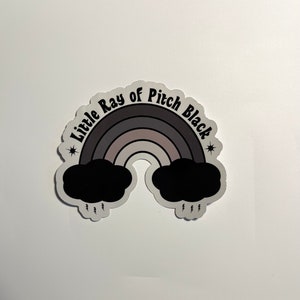 May include: A black and white sticker with a rainbow and the text "Little Ray of Pitch Black" with stars on either side.
