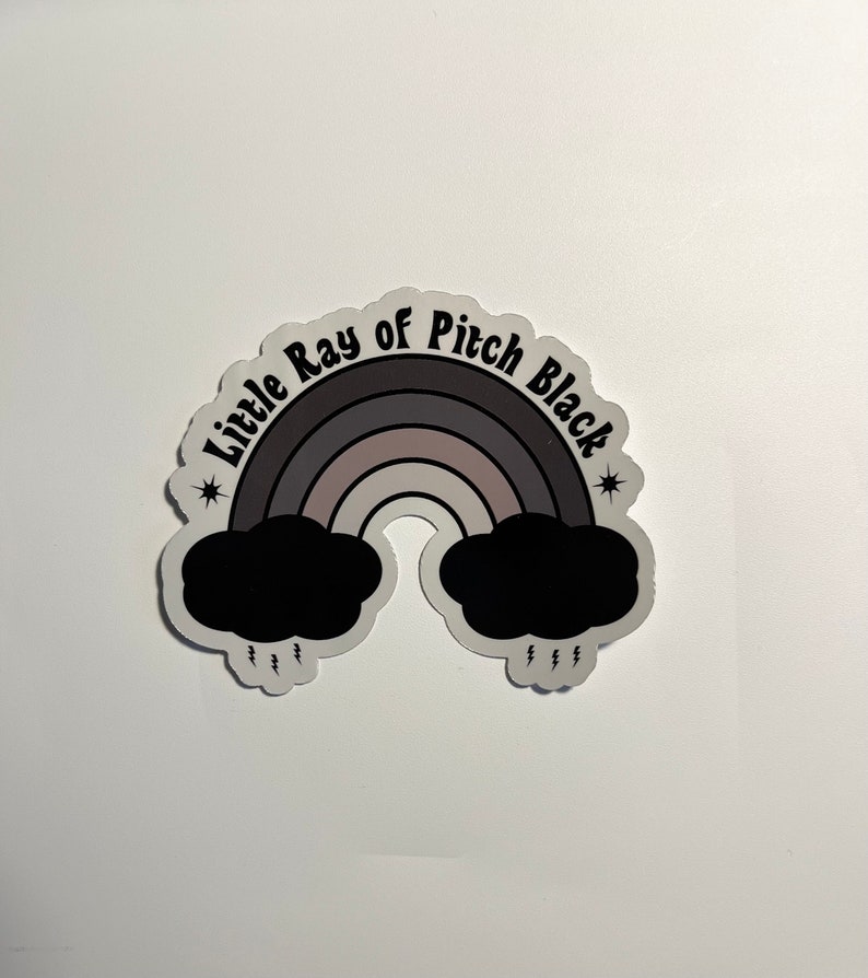 May include: A black and white sticker with a rainbow and the text "Little Ray of Pitch Black" with stars on either side.