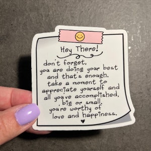May include: White sticker with a pink border and a black and white handwritten message that reads "Hey There! don't forget, you are doing your best and that's enough. take a moment to appreciate yourself and all you've accomplished, big or small, you're worthy of love and happiness."