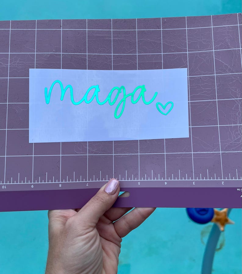 May include: A white sticker with the word "maaga" written in green cursive script with a small heart to the right of the word.