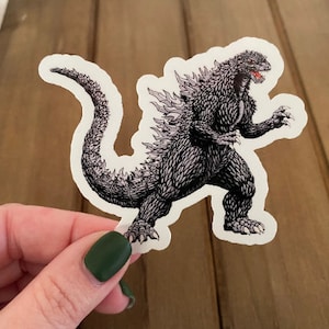 May include: A black and white sticker of a Godzilla-like monster with a white background.