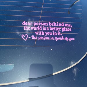 May include: Pink vinyl sticker on a car window with the text "dear person behind me, the world is a better place with you in it. ♡ - the person in front of you"