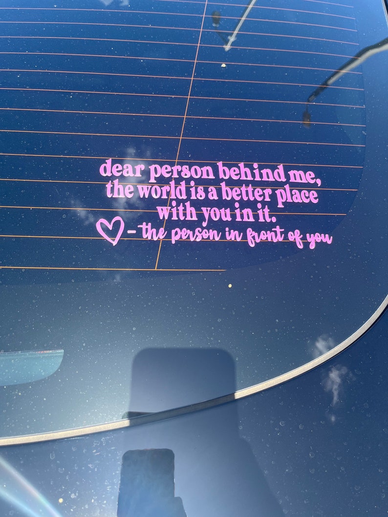 May include: Pink vinyl sticker on a car window with the text "dear person behind me, the world is a better place with you in it. ♡ - the person in front of you"