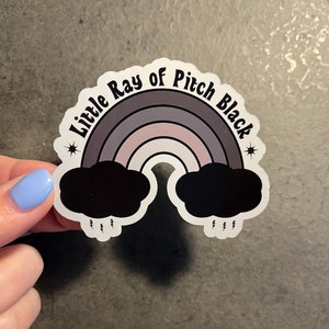 May include: A sticker featuring a rainbow with black clouds at either end and the text "Little Ray of Pitch Black" in a retro font.
