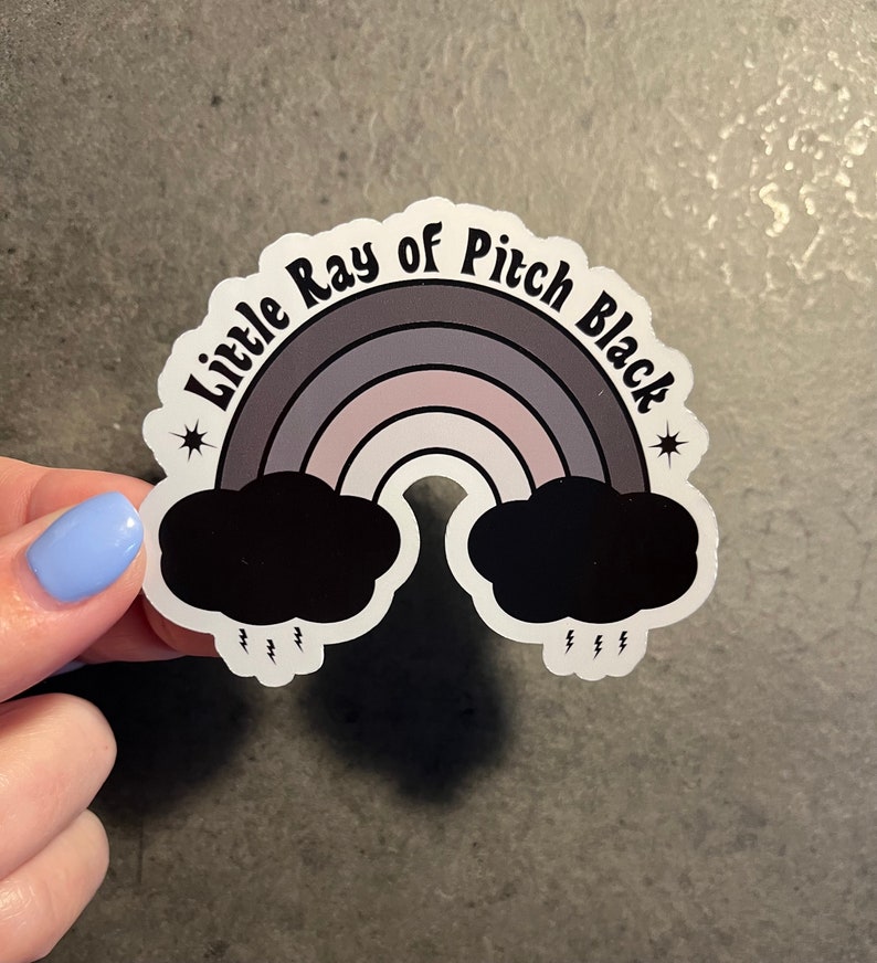 May include: A sticker featuring a rainbow with black clouds at either end and the text "Little Ray of Pitch Black" in a retro font.