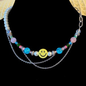 May include: A multi-strand necklace with a yellow smiley face charm, white pearls, pink, blue, and green beads, and silver chains.