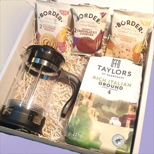 Op de afbeelding: Een cadeaudoos gevuld met een glazen French press koffiezetapparaat, een zak Taylors of Harrogate Rich Italian Ground Roast koffie en drie pakjes Border Biscuits. De koekjes zijn Light & Buttery Viennese Whirls, Divinely Chocolatey Cookies en Sweet Memories Butterscotch Crunch.