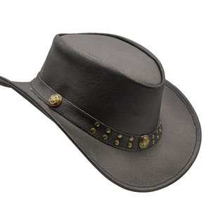 K&ouml;nnte beinhalten: Ein schwarzer Cowboyhut aus Leder mit einem dekorativen Band mit Metallnieten und einem kleinen Metalldesign. Der Hut hat eine breite Krempe und eine hohe Krone.