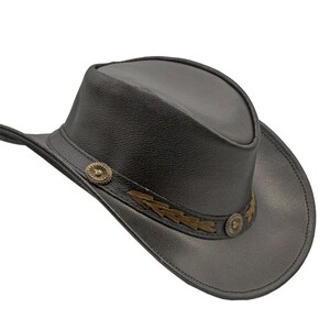 K&ouml;nnte beinhalten: Ein schwarzer Cowboyhut aus Leder mit einem braunen Lederband und goldenen Verzierungen.