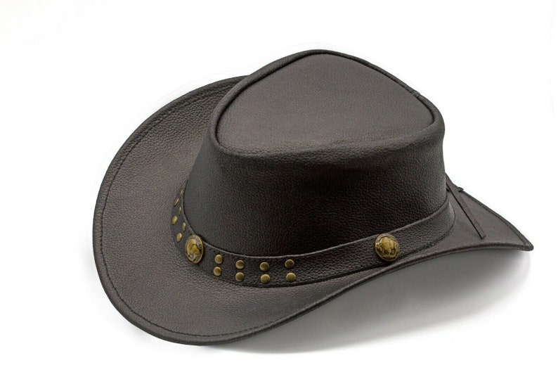 K&ouml;nnte beinhalten: Ein brauner Cowboyhut aus Leder mit breiter Krempe und einem dekorativen Band mit Metallnieten und Verzierungen.