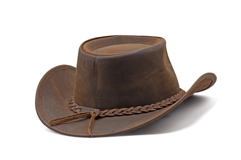 May include: A brown leather cowboy hat with a braided leather band and a leather strap.