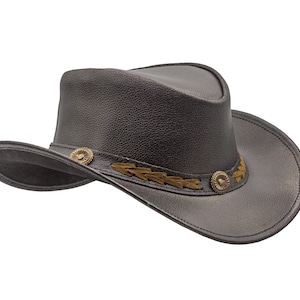 K&ouml;nnte beinhalten: Ein schwarzer Cowboyhut aus Leder mit einem braunen Lederband und Metallverzierungen.