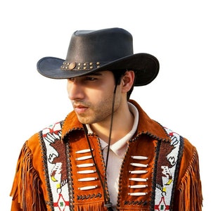 K&ouml;nnte beinhalten: Ein Mann tr&auml;gt einen schwarzen Leder-Cowboyhut mit Perlenbesatz und eine braune Wildlederjacke mit Fransen und Perlenbesatz.