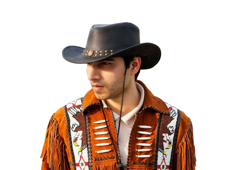 K&ouml;nnte beinhalten: Ein Mann tr&auml;gt einen schwarzen Leder-Cowboyhut mit Perlenbesatz und eine braune Wildlederjacke mit Fransen und Perlenbesatz.