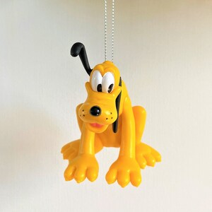 May include: A yellow plastic ornament of Pluto, a cartoon dog from Disney, hanging from a silver string.